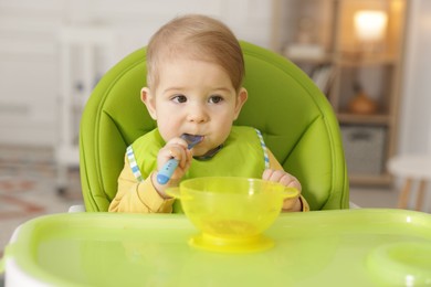 Cute little baby eating healthy food in high chair indoors