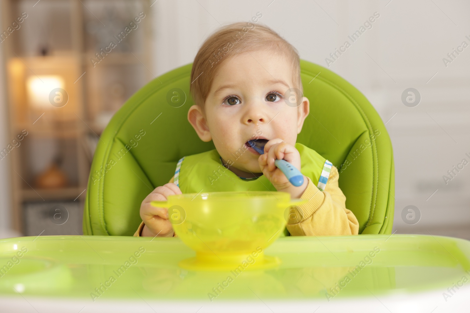 Photo of Cute little baby eating healthy food in high chair indoors