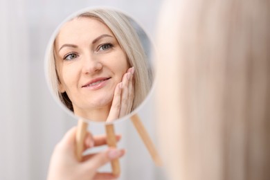 Beautiful woman looking at herself in mirror indoors