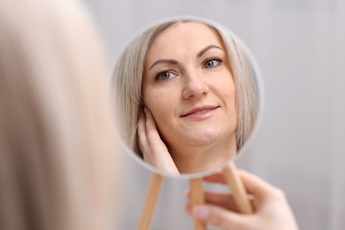 Photo of Beautiful woman looking at herself in mirror indoors