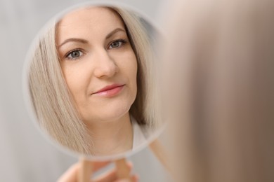 Photo of Beautiful woman looking at herself in mirror indoors