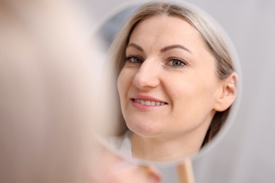 Beautiful woman looking at herself in mirror indoors