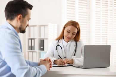 Cardiologist taking notes while consulting patient at table in clinic