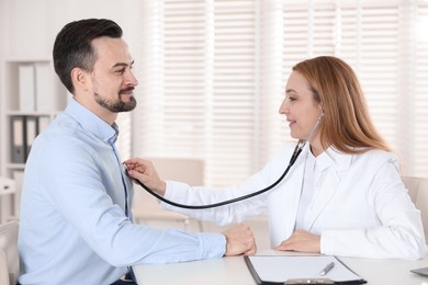 Photo of Cardiologist with stethoscope listening patient's heartbeat at desk in hospital