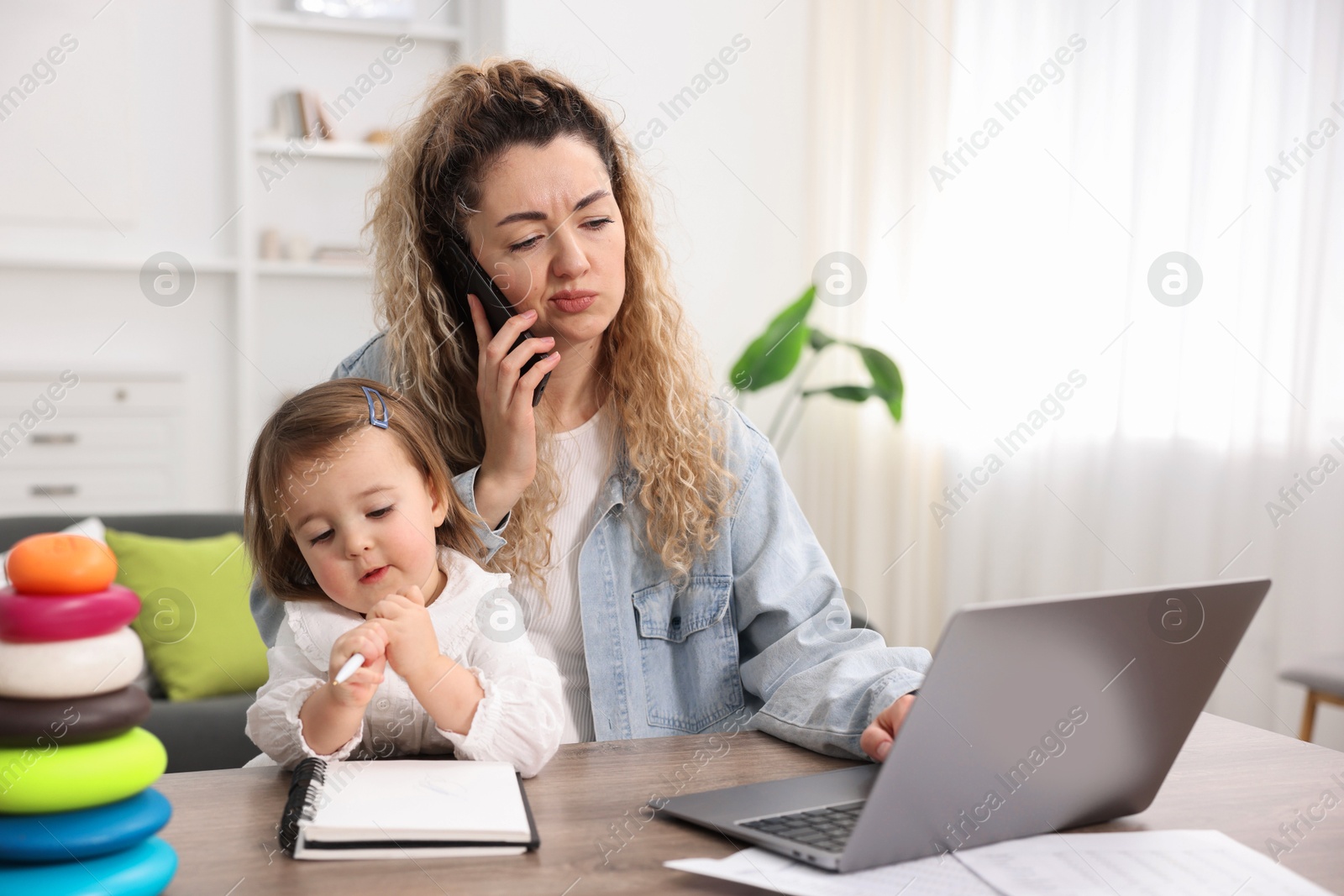 Photo of Work-family balance. Single mother talking on smartphone and her daughter at table indoors