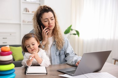 Work-family balance. Single mother talking on smartphone and her daughter at table indoors