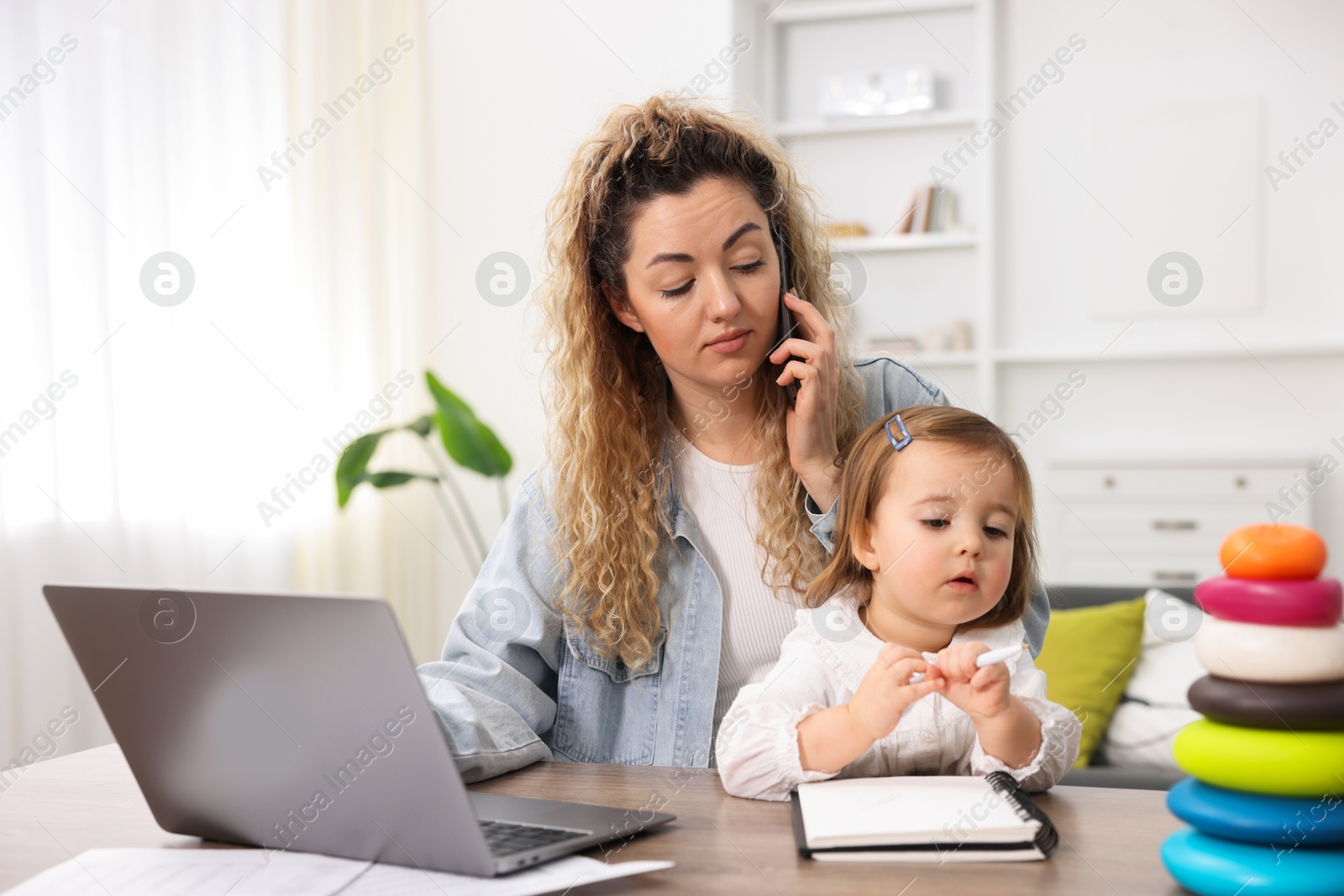 Photo of Work-family balance. Single mother talking on smartphone and her daughter at table indoors