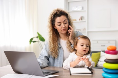 Work-family balance. Single mother talking on smartphone and her daughter at table indoors