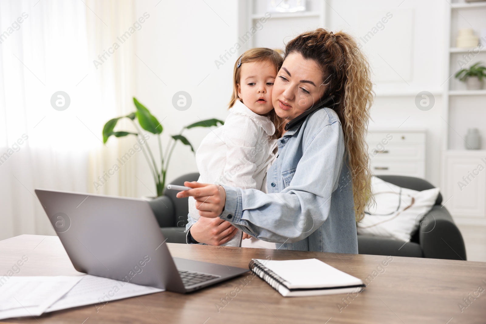 Photo of Single mother holding her daughter while talking on smartphone at table indoors