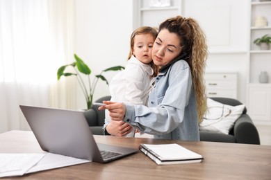 Single mother holding her daughter while talking on smartphone at table indoors