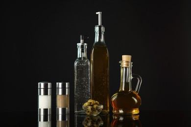 Photo of Salad dressings, spices and olives on mirror surface against black background