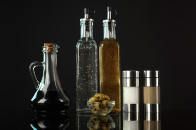 Photo of Salad dressings, spices and olives on mirror surface against black background