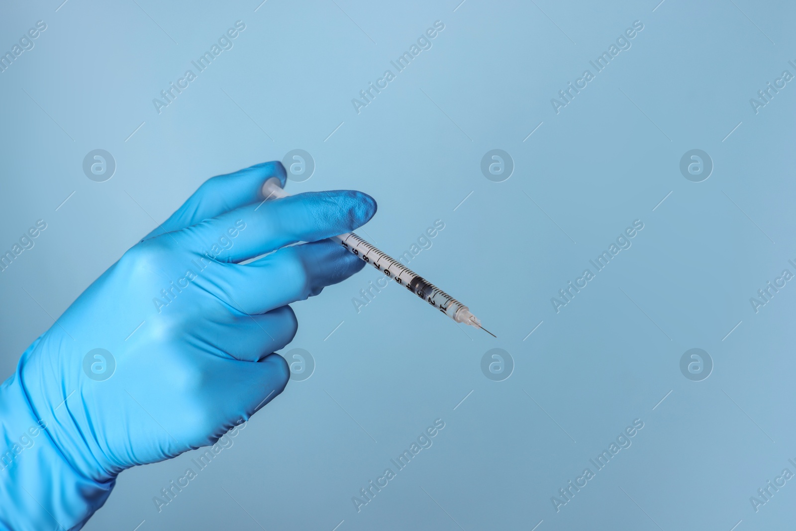 Doctor holding syringe with medication on dusty light blue background, closeup. Space for text Photo of Doctor holding syringe with medication on dusty light blue background, closeup. Space for text