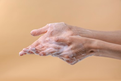 Photo of Woman washing hands with foaming soap on beige background, closeup. Hygiene