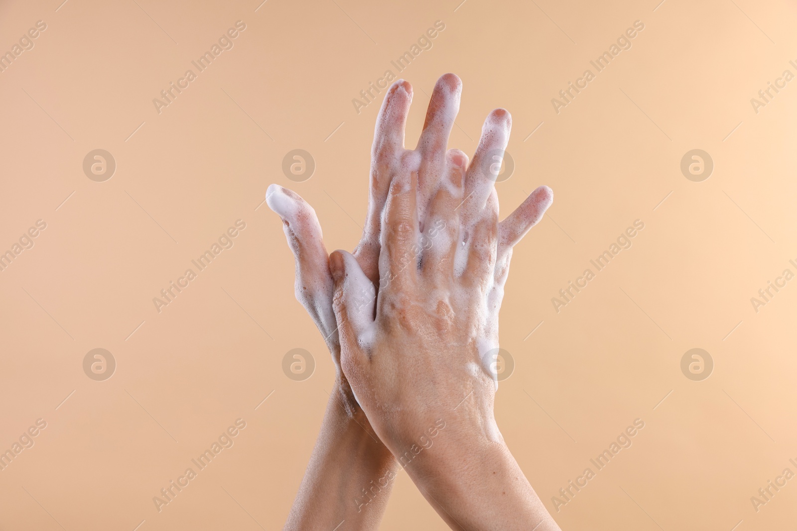 Photo of Woman washing hands with foaming soap on beige background, closeup. Hygiene