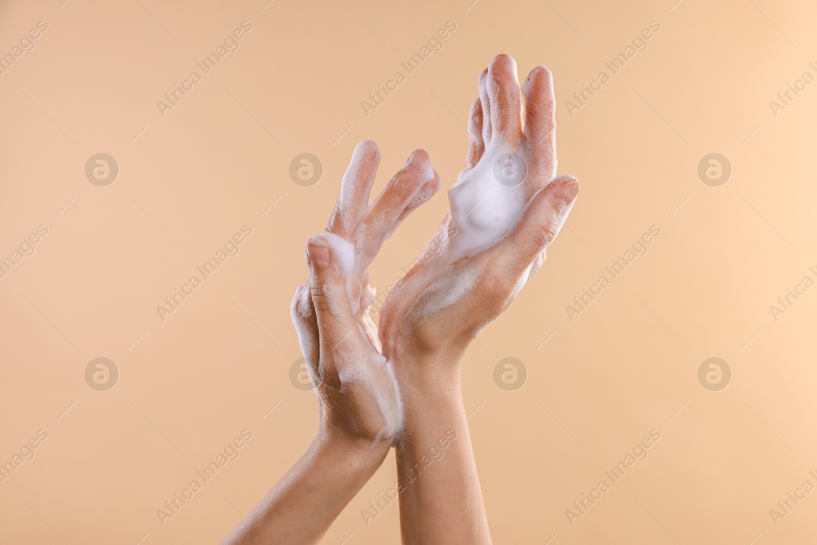 Photo of Woman washing hands with foaming soap on beige background, closeup. Hygiene