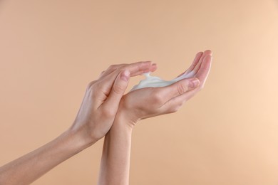 Woman washing hands with foaming soap on beige background, closeup. Hygiene