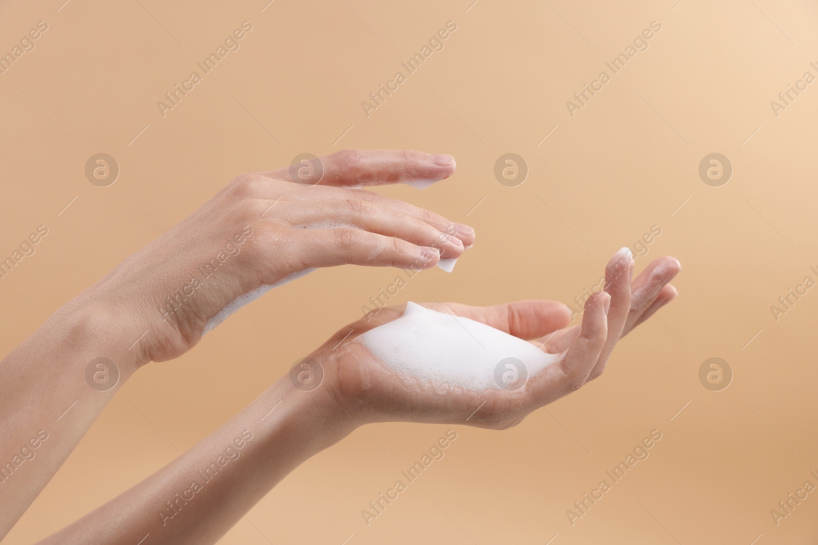 Photo of Woman washing hands with foaming soap on beige background, closeup. Hygiene