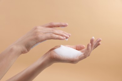 Woman washing hands with foaming soap on beige background, closeup. Hygiene