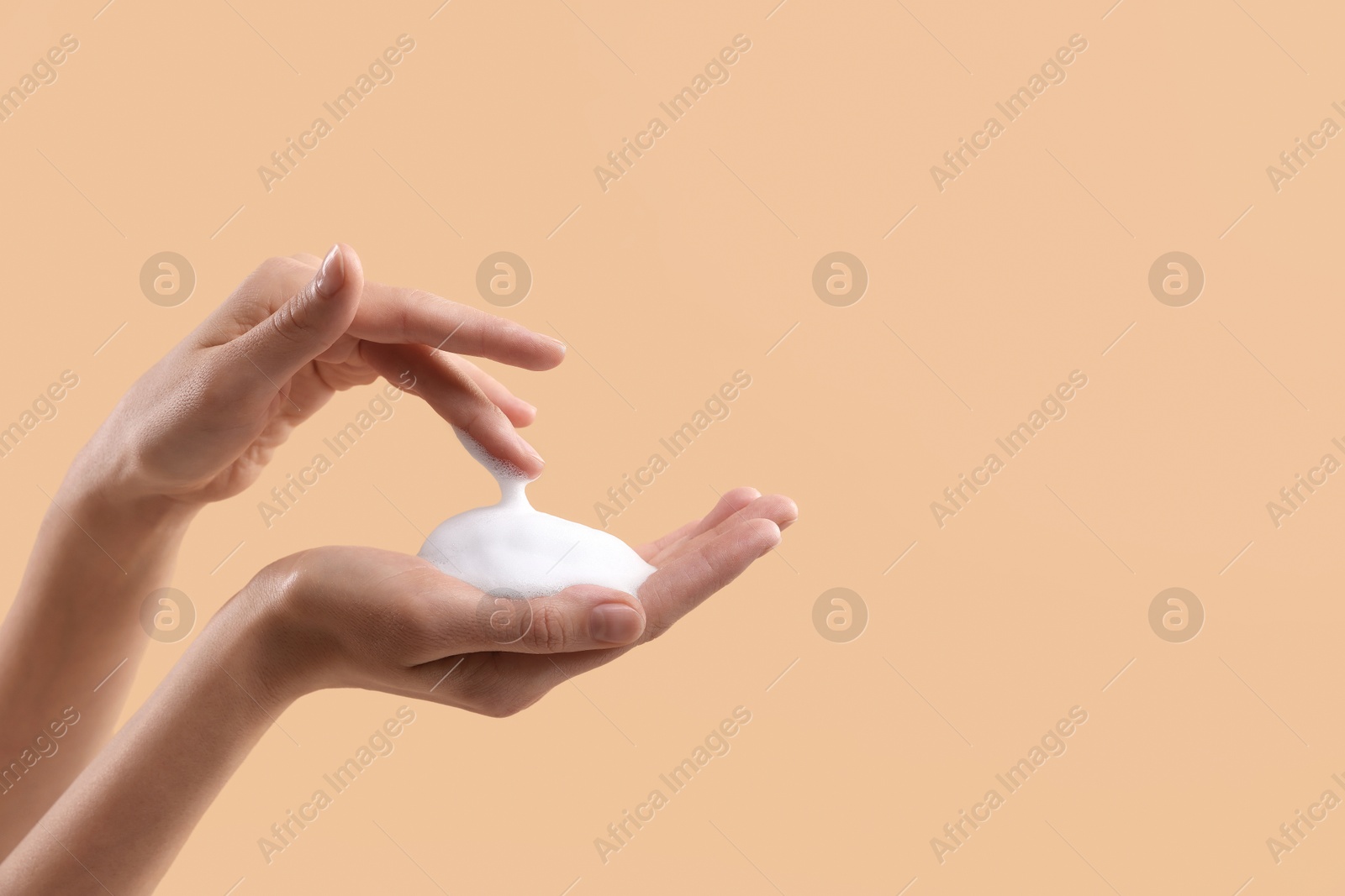 Photo of Woman washing hands with foaming soap on beige background, closeup with space for text. Hygiene