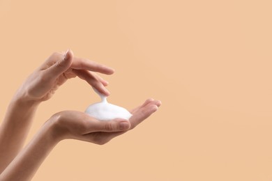 Woman washing hands with foaming soap on beige background, closeup with space for text. Hygiene