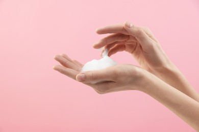 Woman washing hands with foaming soap on pink background, closeup. Hygiene