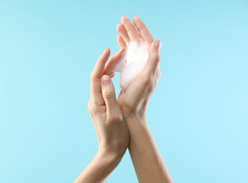 Woman washing hands with foaming soap on light blue background, closeup. Hygiene