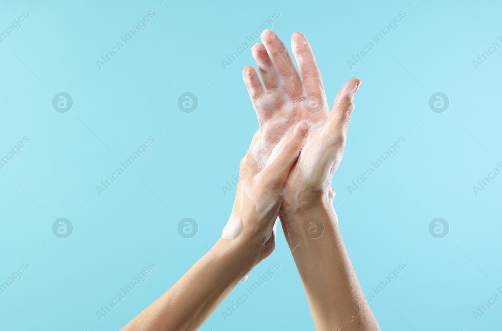 Photo of Woman washing hands with foaming soap on light blue background, closeup. Hygiene