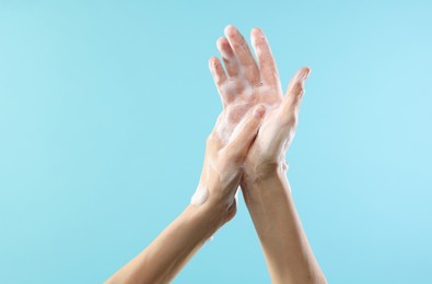 Woman washing hands with foaming soap on light blue background, closeup. Hygiene