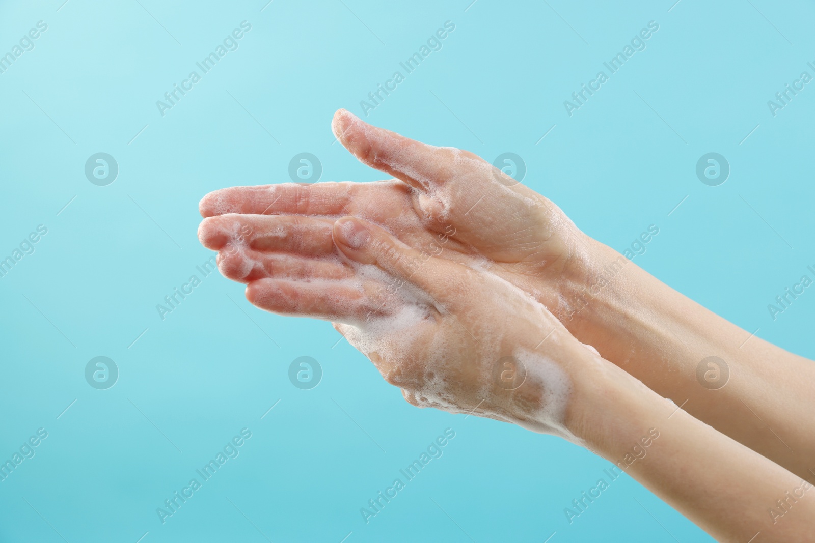 Photo of Woman washing hands with foaming soap on light blue background, closeup. Hygiene