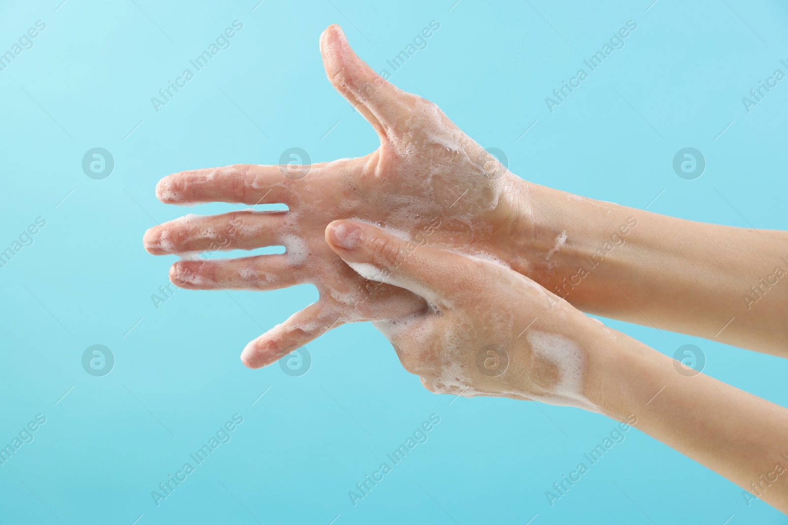 Photo of Woman washing hands with foaming soap on light blue background, closeup. Hygiene