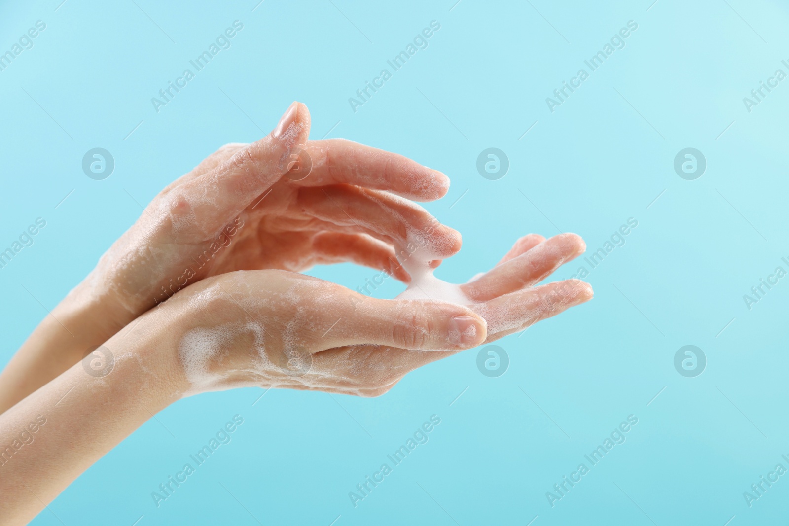 Photo of Woman washing hands with foaming soap on light blue background, closeup. Hygiene