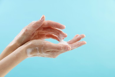 Woman washing hands with foaming soap on light blue background, closeup. Hygiene