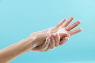 Woman washing hands with foaming soap on light blue background, closeup. Hygiene