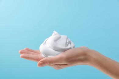 Woman with cosmetic foam on light blue background, closeup