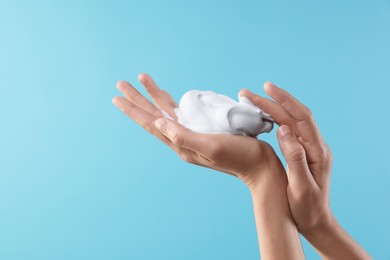 Woman with cosmetic foam on light blue background, closeup with space for text