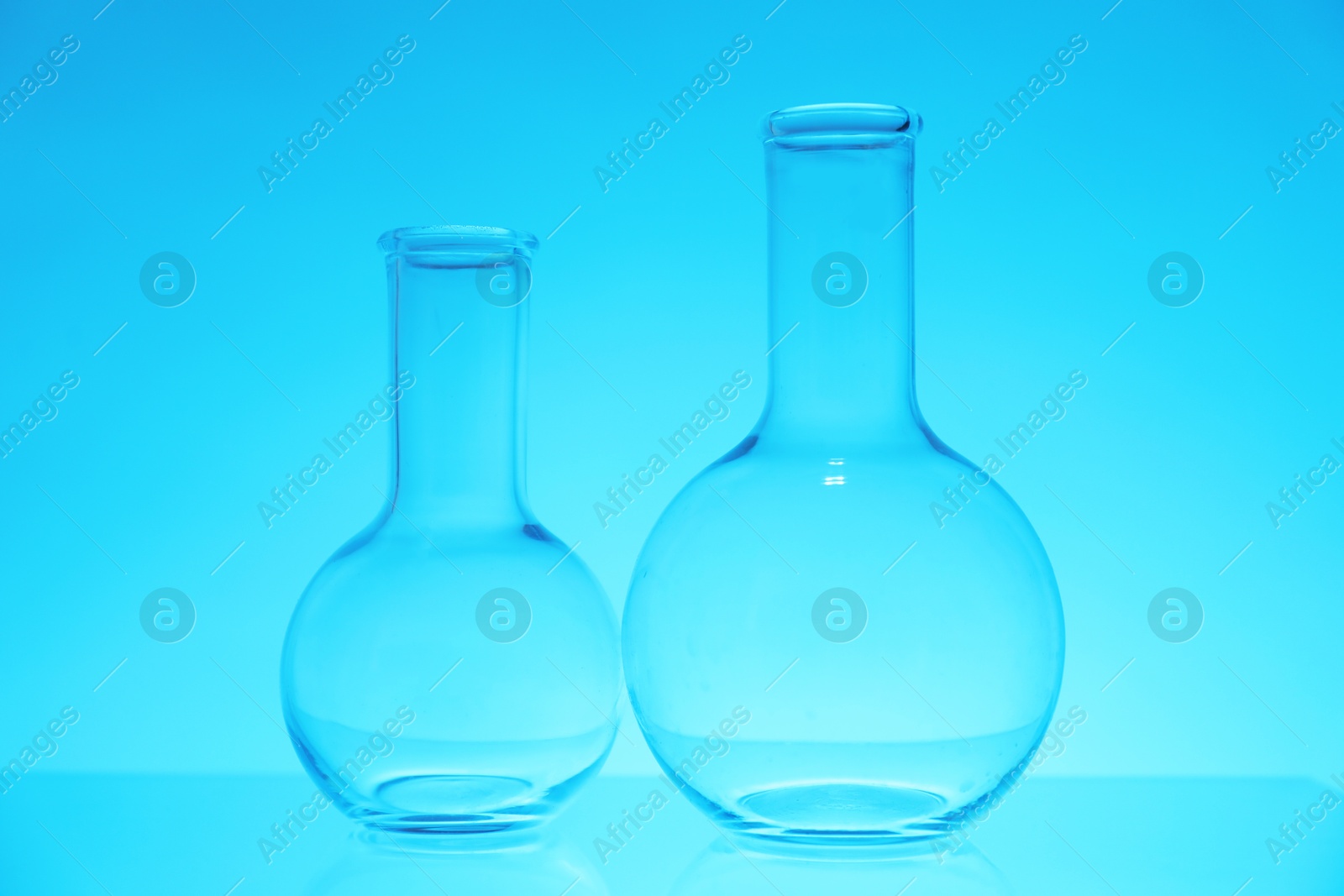 Photo of Empty flasks on light blue background. Laboratory equipment