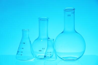 Photo of Empty flasks on light blue background. Laboratory equipment