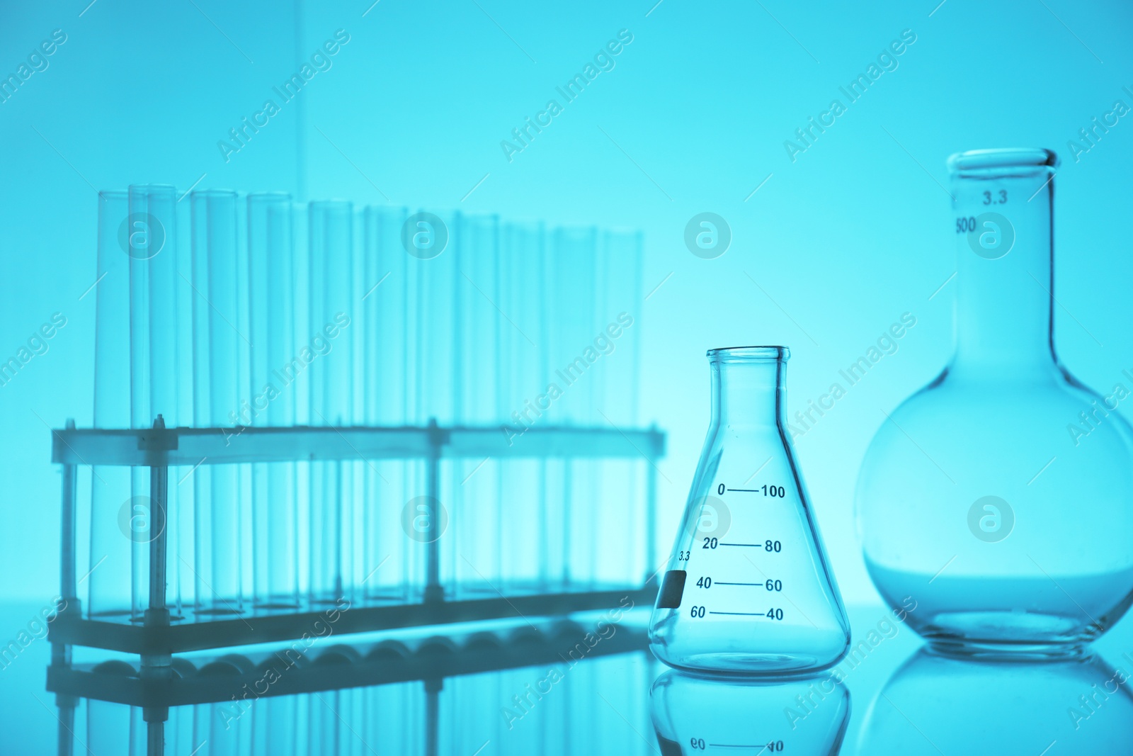 Photo of Laboratory glassware on mirror surface against light blue background