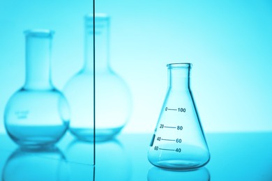 Photo of Empty flasks on mirror surface against light blue background. Laboratory equipment