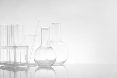 Photo of Laboratory glassware on mirror surface against light background, space for text