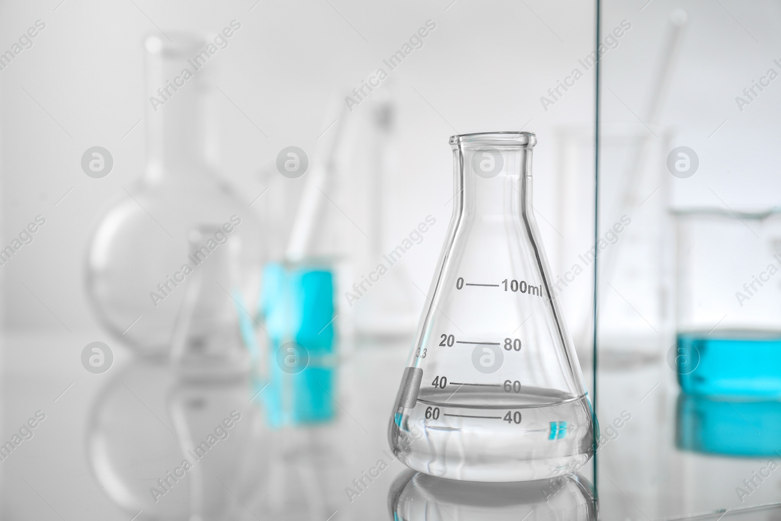 Photo of Flask with liquid on mirror surface against light background. Laboratory glassware