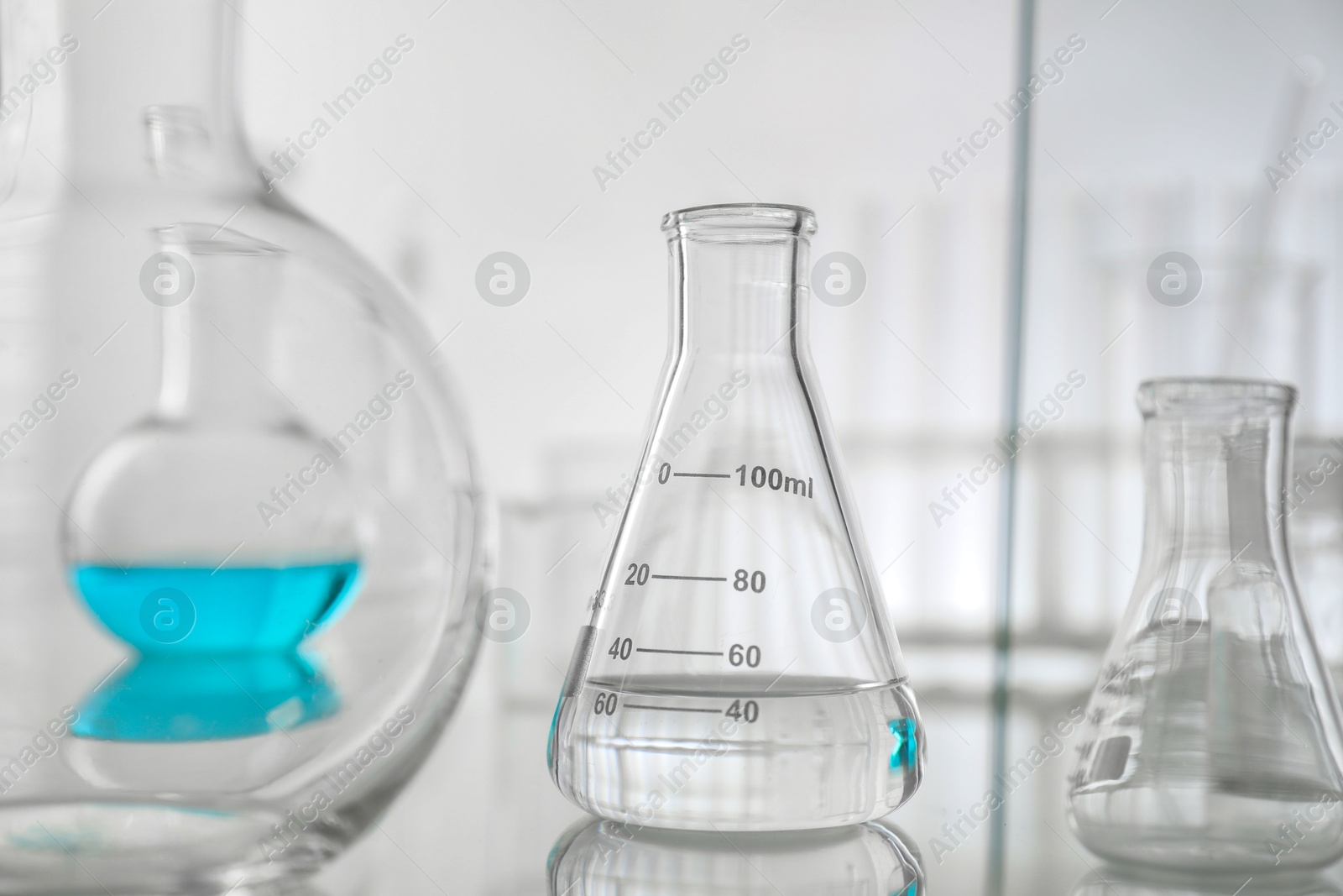 Photo of Flask with liquid on mirror surface against light background. Laboratory glassware