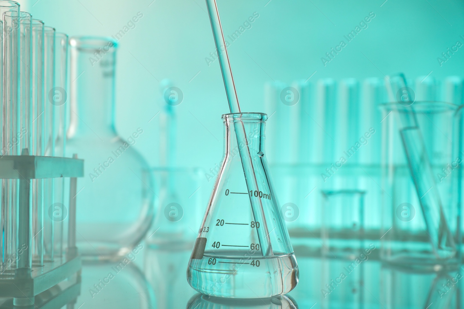 Photo of Laboratory glassware on mirror surface against turquoise background