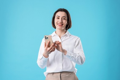 Photo of Smiling secretary using smartphone on light blue background