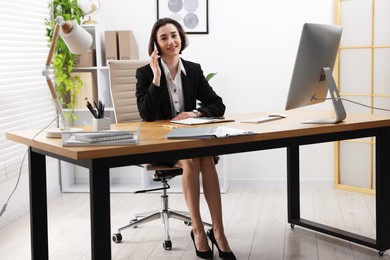 Secretary talking on smartphone while working at table in office