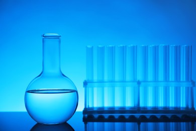 Photo of Laboratory glassware with liquid on mirror surface against light blue background