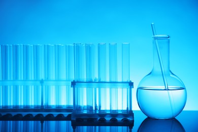 Laboratory glassware with liquid on mirror surface against light blue background