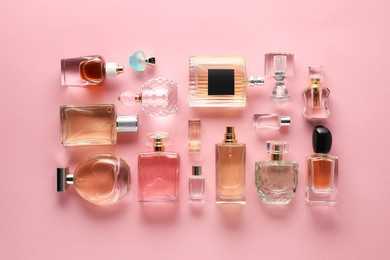 Photo of Bottles of various perfumes on pink background, flat lay