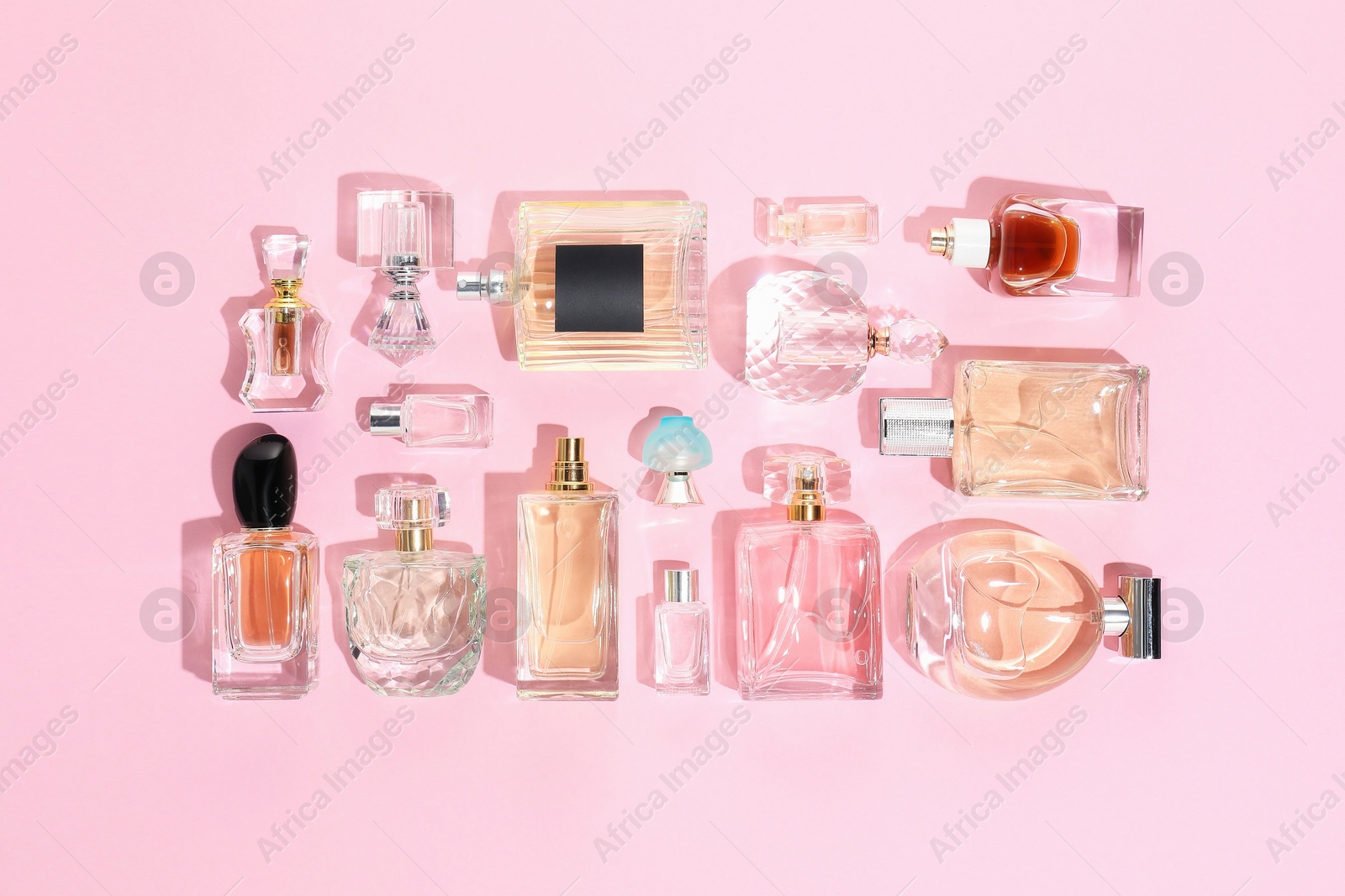 Bottles of various perfumes on pink background, flat lay Photo of Bottles of various perfumes on pink background, flat lay